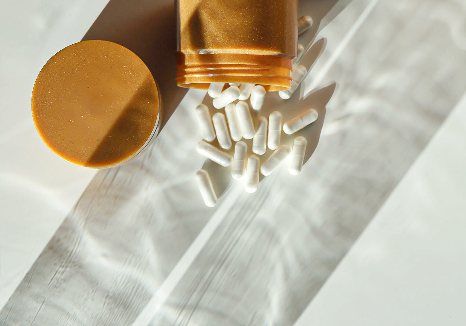 Styling and studio photography presenting a jar of supplements on a white background and artistic shadows.